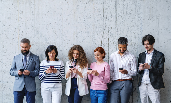 Entrepreneurs standing against concrete wall indoors in office, using smartphone. - Stock Photo - Images