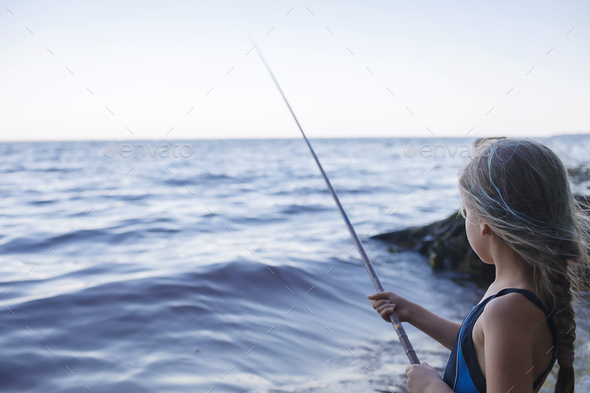 Girl in swimming wear fishing from sea beach in early morning, blue hours, active weekend, camping - Stock Photo - Images