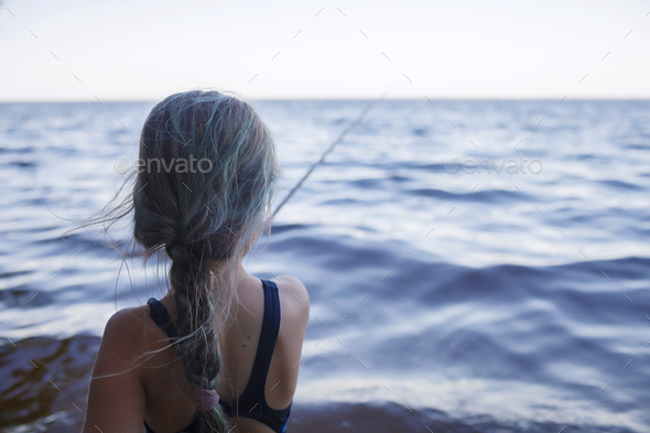Girl in swimming wear fishing from sea beach in early morning, blue hours, active weekend, camping - Stock Photo - Images
