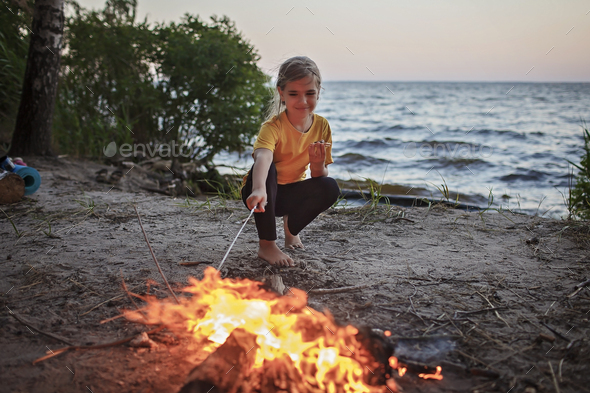 Girl roasting marshmallow to make smores over fire flame during camping, traditional travel food - Stock Photo - Images