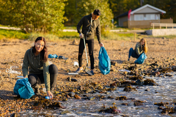 Young woman in a team picking up plastic garbage in bag at beach - Stock Photo - Images