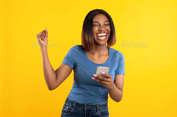 Happy Black Lady Holding Phone Gesturing Yes Over Yellow Background