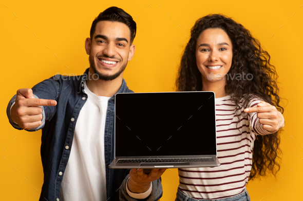 Great Website. Smiling middle eastern couple pointing at laptop with black screen