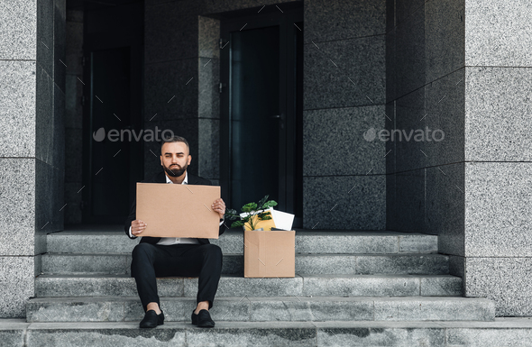 Unemployment concept. Depressed mature businessman sitting with empty cardboard sign and box of - Stock Photo - Images