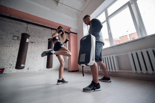 Female martial arts fighter practicing leg kick or high kick with her trainer in a boxing studio at