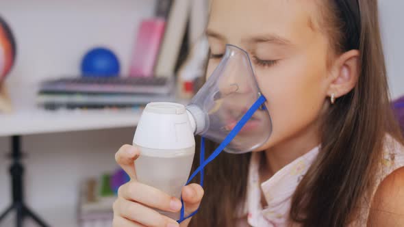 Little Girl Makes Inhalation with Medical Nebulizer While Sitting at the Table