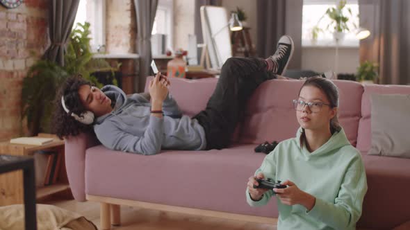 Teen Kids Using Smartphone and Playing Console Game at Home alt