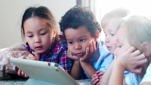 Mixed Raced Little Children Lying on Bed and Watching Cartoon on Tablet