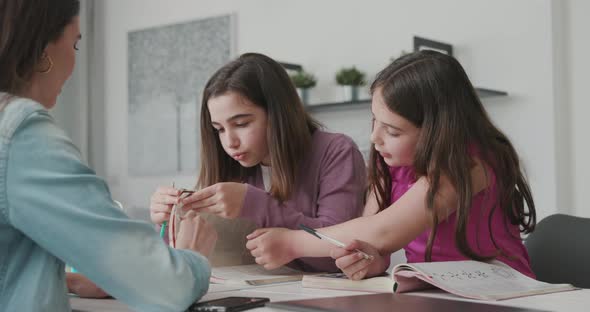 Woman helping children with their homework, they are sitting at desk and studying together