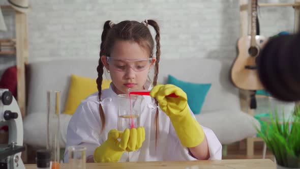 Teen Blogger in a White Coat and Glasses in the Laboratory Mixes the Reagents alt