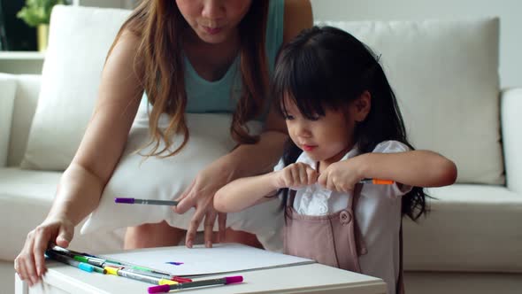 Young mother helping her daughter open colour pencil