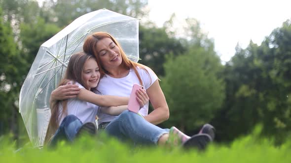 Happy mother smiles and plays with her daughter in the park hiding from the rain. alt