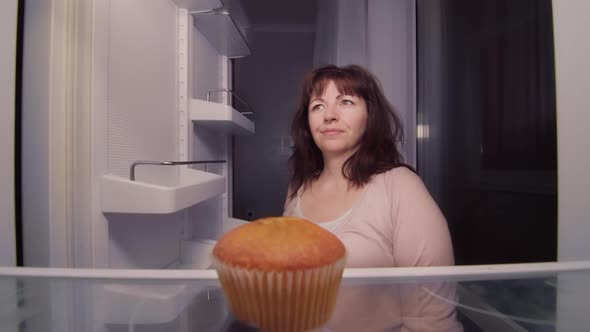 Woman Takes a Cupcake From the Refrigerator at Night