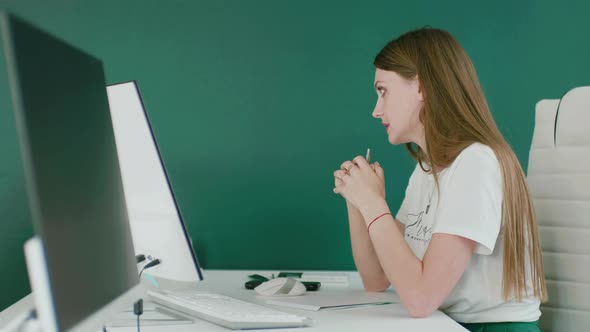 Side View of a Woman Talking in the Office Sitting at a Desk with a Monitor
