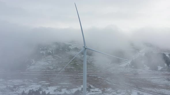 Wind turbine in a snowy landscape with early winter morning mist. alt
