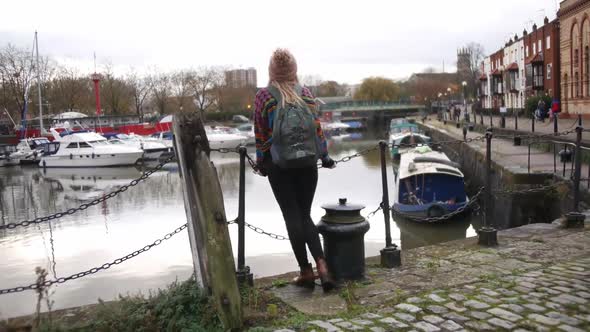 woman smiling into the camera and then starts looking at the waterside of Bristol harbour. alt