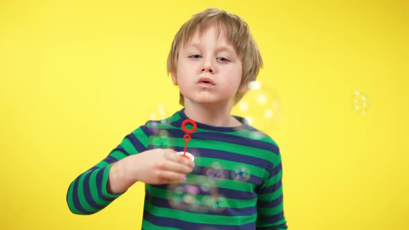 Portrait of Happy Relaxed Boy Blowing Soap Bubbles at Yellow Background alt