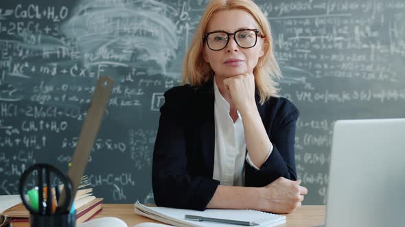 Serious Adult Woman Sitting at Desk in University Classroom Looking at Camera alt
