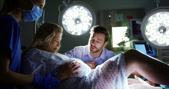 Doctor examining pregnant woman during delivery while man holding her hand in operating room alt