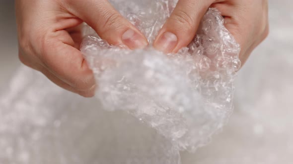 Female Hands Burst Air Bubbles on Bubble Wrap on a White Background alt