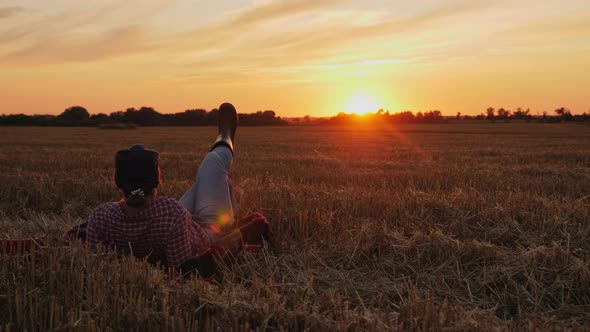 Woman Farmer Resting on Straw in a Field at Sunset alt