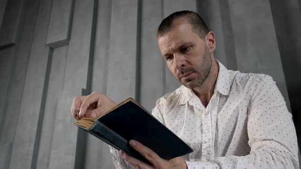 A Man is Reading an Old Book in a Dark Modern Interior