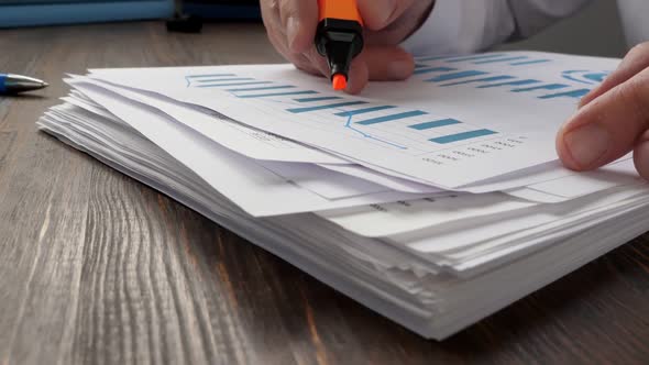 A Stack of Paper and a Closeup of Hands Making Notes with a Marker on a Financial Report