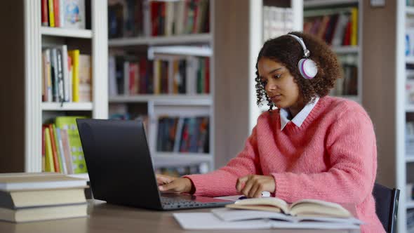 Black Girl Studying in Library and Browsing Internet on Laptop alt