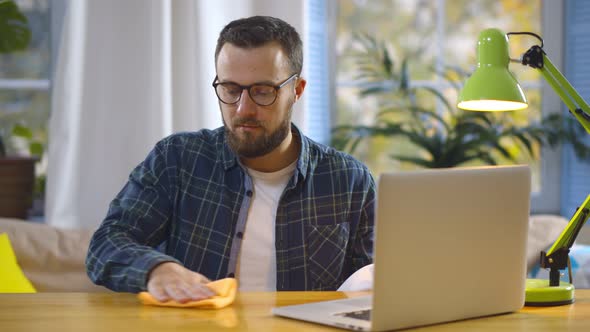 Young Man Cleaning Desktop with Detergent Sprayer and Cloth Before Start Working at Home Office alt