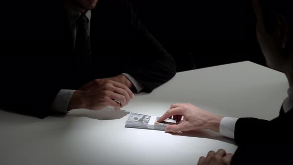 Businessman giving bribe money to his partner in dark room after making a deal