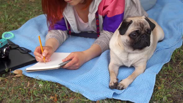 Girl Laying on a Lawn and Writing Her Pug Laying Beside
