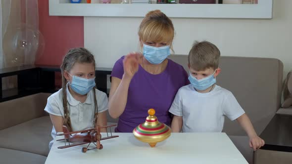 Mom Shows Children in Medical Masks How To Spin an Old Top. Social Distancing and Self-isolation in