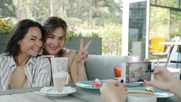 Crazy Young Women Having Fun in Cafe Laughing Dancing Posing for Smartphone Camera alt