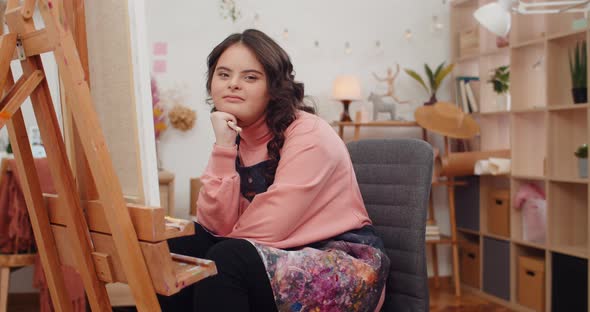 Portrait of Cheerful Young Girl with Down Syndome Holding Paint Brush and Looking To Camera. Preety alt