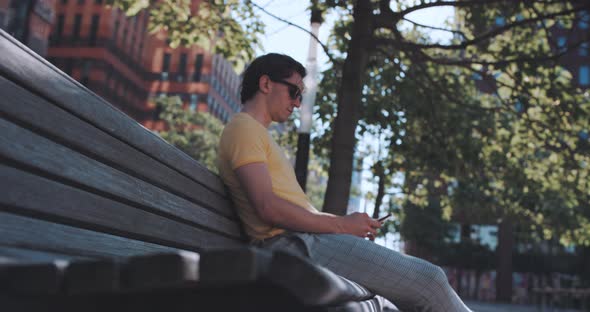 Man sits on park bench while using phone alt