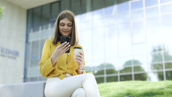 Joyful Businesswoman Browsing Internet on Phone Drinking Coffee Spending Time Outdoors alt