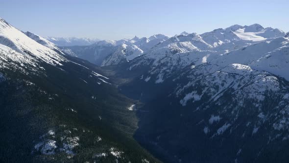 Creek Flowing Between Snowy Mountain Ranges Around Garibaldi In British Columbia, Canada - Aerial Dr alt