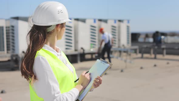 Portrait of a Young Woman Engineer Who is Making Entries in Documents and Watching the Engineer's alt