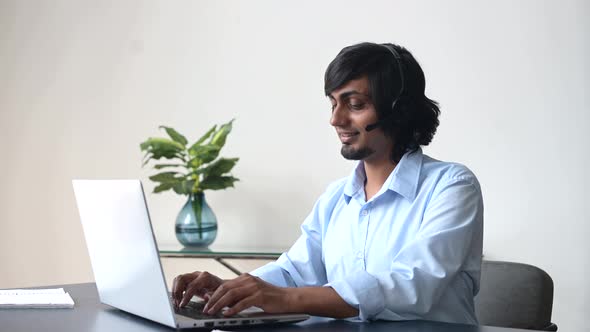 Headshot of Smiling Indian Male Employee Wearing Headset Takes a Call