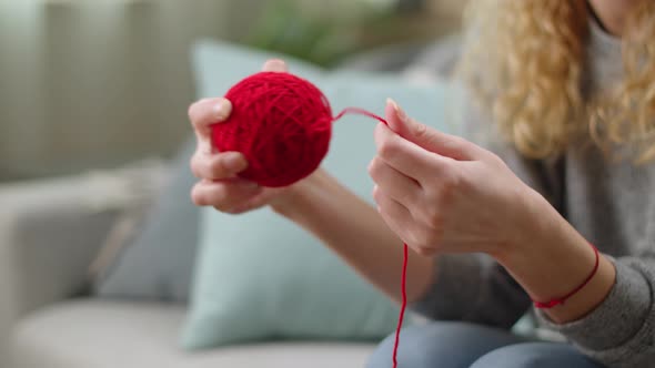 Hands of a Young Girl Wind Up Red Threads for Knitting Into a Ball alt