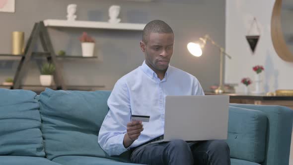 African Man Making Online Payment Failure on Laptop on Sofa alt