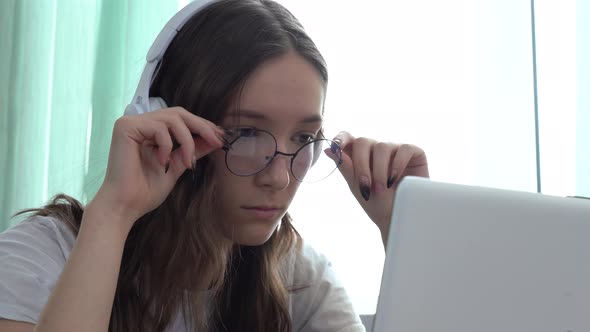 Serious Caucasian Girl Wearing Headphones and Watching an Educational Video Course with Her Laptop alt