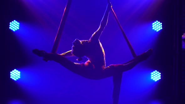 Young Woman Doing Show Acrobatic Trick on Air Silk. Exciting Acrobatic Show in a Dark Studio with alt