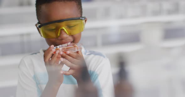 Video of happy african american boy wearing glasses and holding reagent during chemistry lesson alt