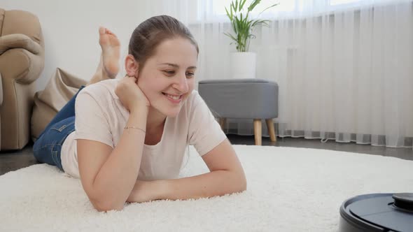 Happy Smiling Woman with Working Robot Vacuum Cleaner on Flooar at Living Room alt