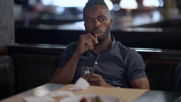 Handsome Relaxed Confident African American Man Eating Roasted Chicken Legs Sitting with Beer in alt