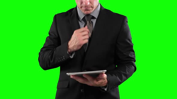 a Caucasian man in suit using a tablet in a green background