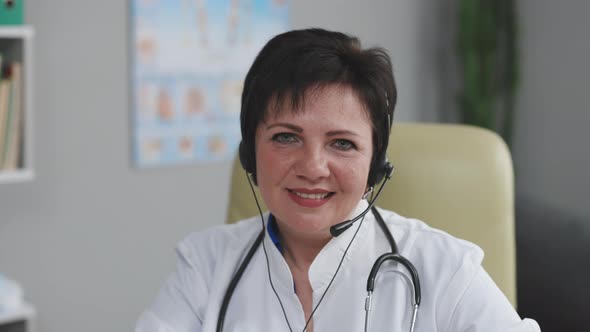 Successful Physician in White Lab Coat Wears Headset Looks at the Camera and Smiles in Hospital alt