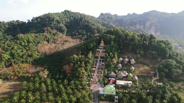 aerial drone of a unique temple with a golden buddha on a mountain surrounded by coconut trees in Ao alt