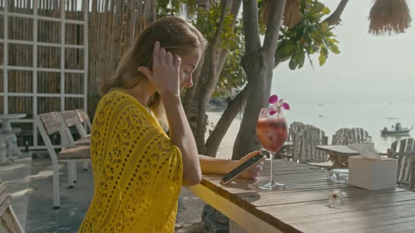 A Pretty Young Woman with Vitiligo Pigmentation Sits By the Beach Chatting on the Phone alt